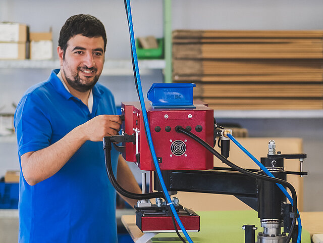 Ein Mann in einem blauen Hemd bedient eine rote Industriemaschine in einer Werkstattumgebung.